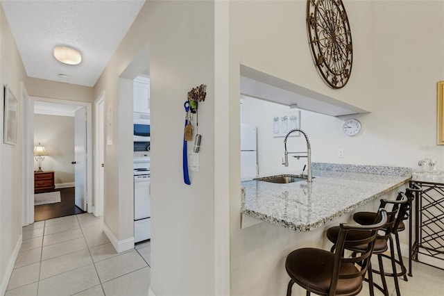 kitchen featuring sink, light tile patterned floors, light stone counters, white appliances, and a textured ceiling