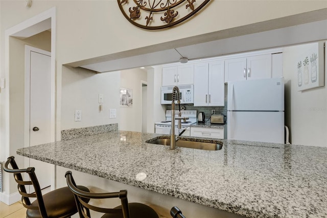 kitchen featuring white appliances, light stone countertops, white cabinetry, a kitchen breakfast bar, and kitchen peninsula