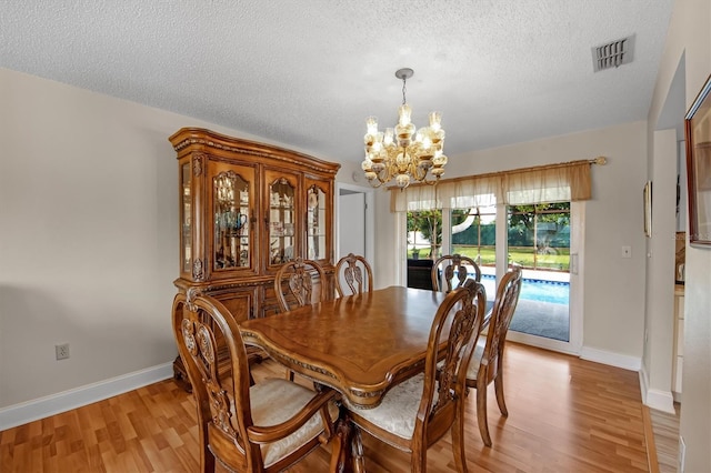 dining area with a textured ceiling, a notable chandelier, and light hardwood / wood-style floors