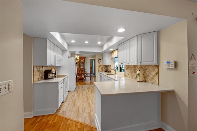 kitchen with kitchen peninsula, a raised ceiling, white cabinets, white appliances, and backsplash