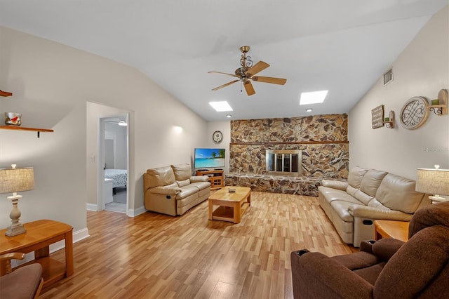 living room with a stone fireplace, lofted ceiling with skylight, light hardwood / wood-style floors, and ceiling fan