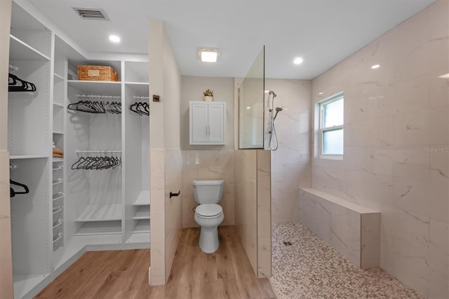 bathroom with tile walls, wood-type flooring, toilet, and tiled shower