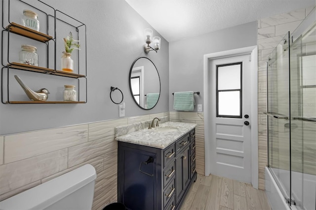 full bathroom with enclosed tub / shower combo, tile walls, vanity, a textured ceiling, and toilet