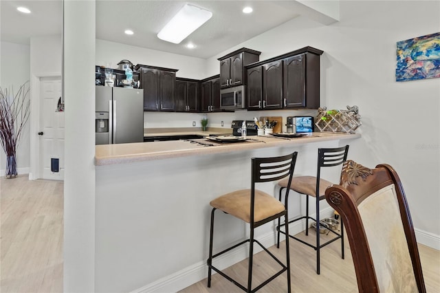 kitchen with a breakfast bar, light hardwood / wood-style floors, kitchen peninsula, and appliances with stainless steel finishes