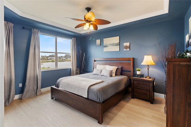 bedroom featuring a water view, light wood-type flooring, and a tray ceiling