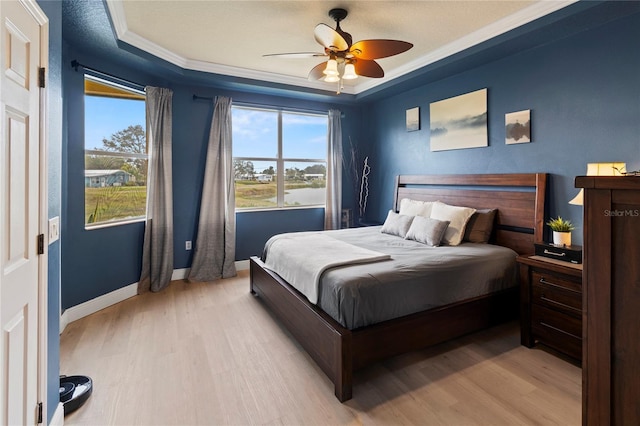 bedroom with multiple windows, a tray ceiling, light hardwood / wood-style floors, and ceiling fan