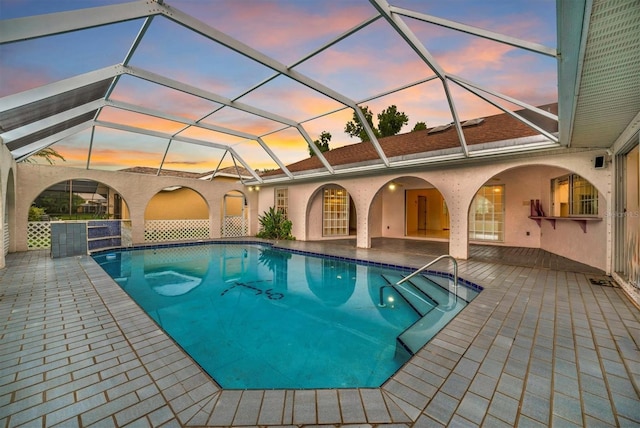 pool at dusk with a lanai and a patio area