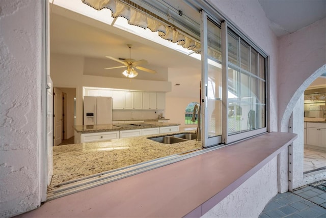 kitchen featuring sink, white cabinetry, light stone counters, white fridge with ice dispenser, and kitchen peninsula