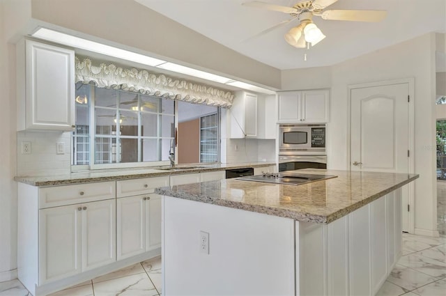 kitchen with stainless steel appliances, light stone countertops, a kitchen island, and white cabinets