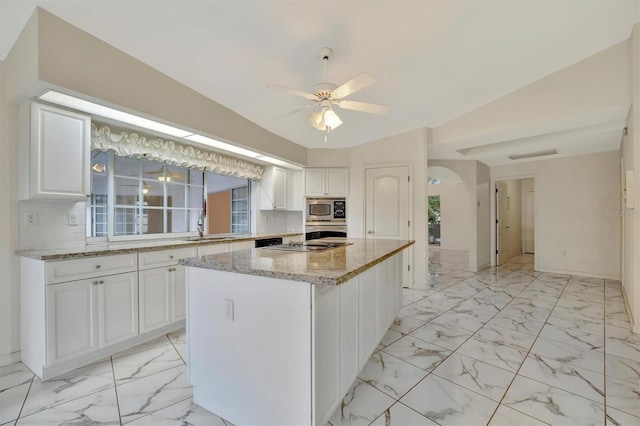 kitchen featuring white cabinetry, vaulted ceiling, a kitchen island, stainless steel appliances, and light stone countertops