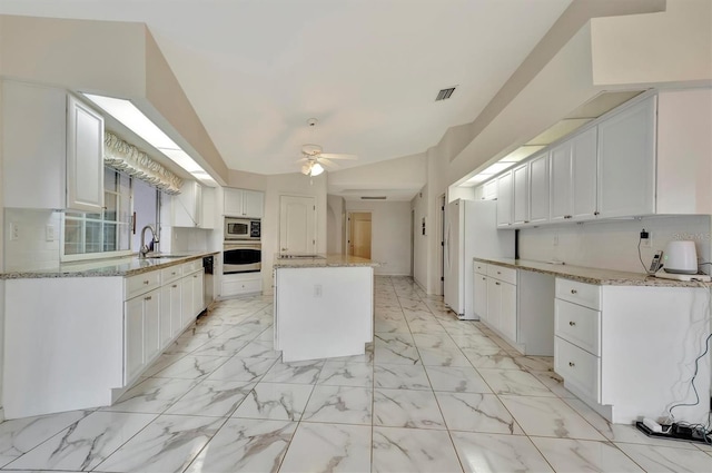 kitchen with appliances with stainless steel finishes, white cabinetry, sink, a center island, and light stone countertops