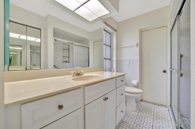 bathroom with a skylight, tile walls, vanity, toilet, and a shower with door