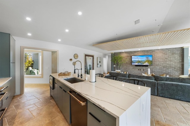 kitchen with brick wall, an island with sink, sink, stainless steel appliances, and light stone countertops