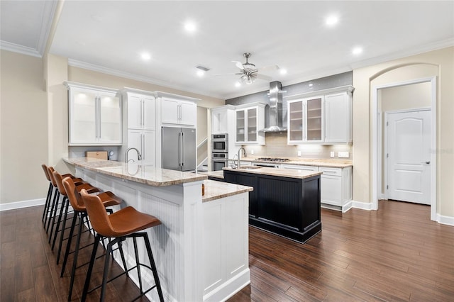 kitchen featuring white cabinetry, appliances with stainless steel finishes, wall chimney exhaust hood, and a kitchen island with sink