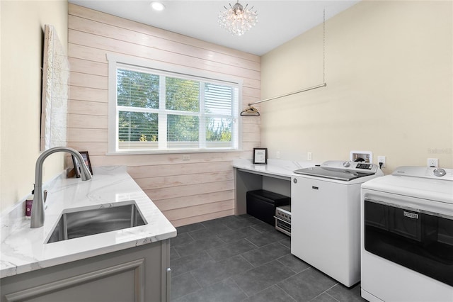 washroom featuring dark tile patterned flooring, sink, wood walls, a notable chandelier, and independent washer and dryer