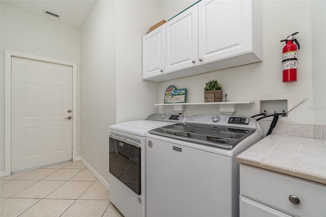 laundry room featuring washer and clothes dryer, light tile patterned floors, and cabinets