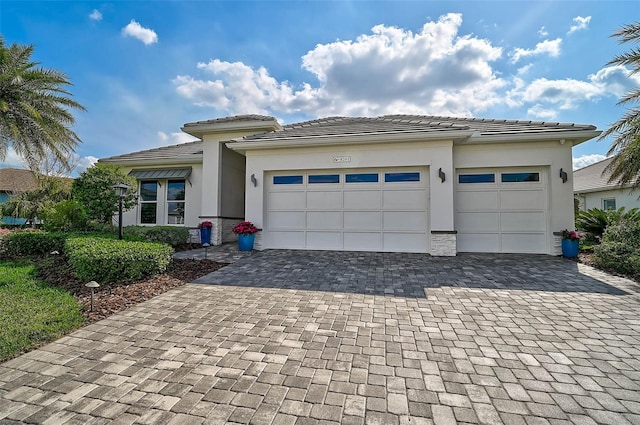 prairie-style home with a garage, a tile roof, decorative driveway, and stucco siding