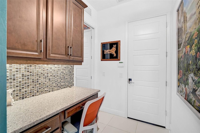 kitchen featuring light tile patterned floors, tasteful backsplash, baseboards, light stone countertops, and built in desk