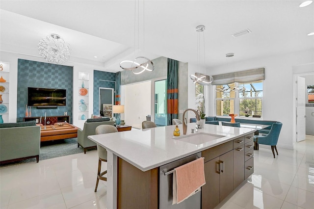 kitchen featuring a sink, open floor plan, hanging light fixtures, light countertops, and an island with sink