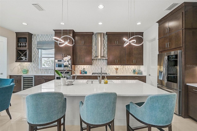 kitchen featuring pendant lighting, stainless steel appliances, visible vents, a kitchen island with sink, and wall chimney exhaust hood