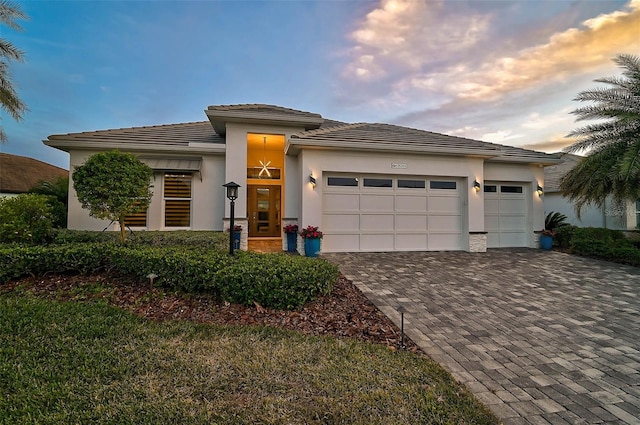 prairie-style home featuring an attached garage, decorative driveway, and stucco siding