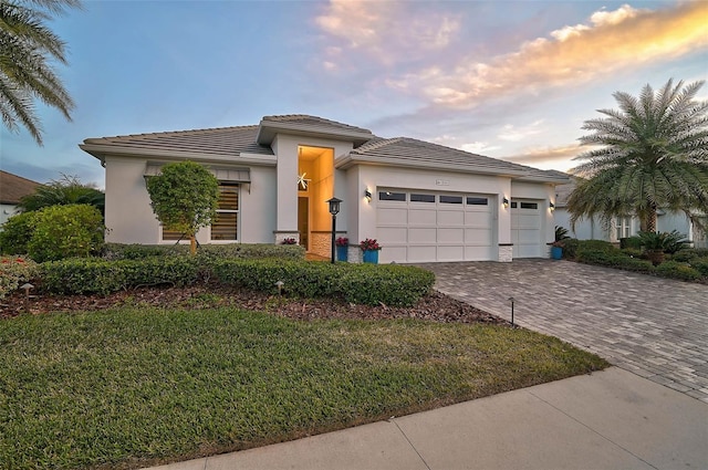 prairie-style house with a tiled roof, an attached garage, decorative driveway, a front yard, and stucco siding