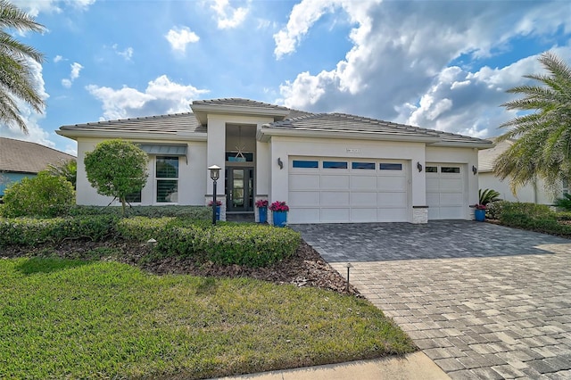 prairie-style home with decorative driveway, an attached garage, a tile roof, and stucco siding