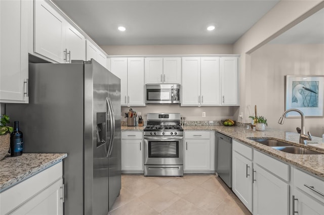 kitchen with light stone countertops, appliances with stainless steel finishes, light tile patterned floors, sink, and white cabinets