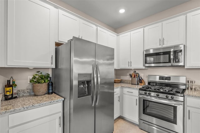 kitchen featuring white cabinets, stainless steel appliances, light stone countertops, and light tile patterned flooring