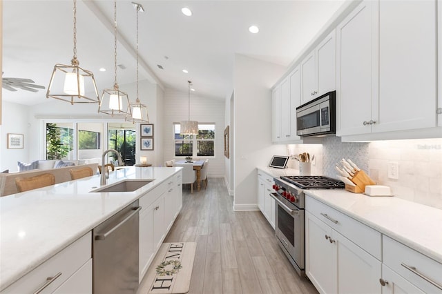 kitchen with pendant lighting, white cabinets, appliances with stainless steel finishes, sink, and vaulted ceiling