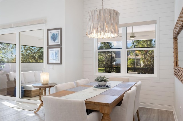 dining area with ceiling fan with notable chandelier, wood-type flooring, and wooden walls