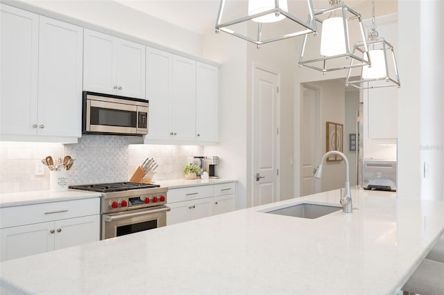 kitchen with pendant lighting, white cabinetry, stainless steel appliances, tasteful backsplash, and sink