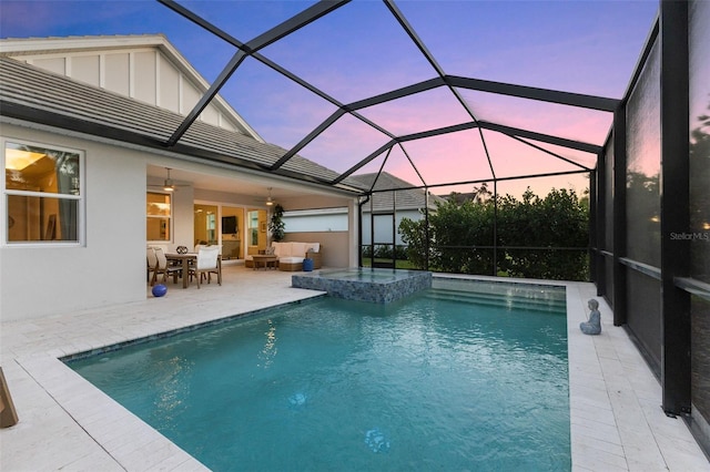 pool at dusk featuring glass enclosure, a patio area, outdoor lounge area, and an in ground hot tub