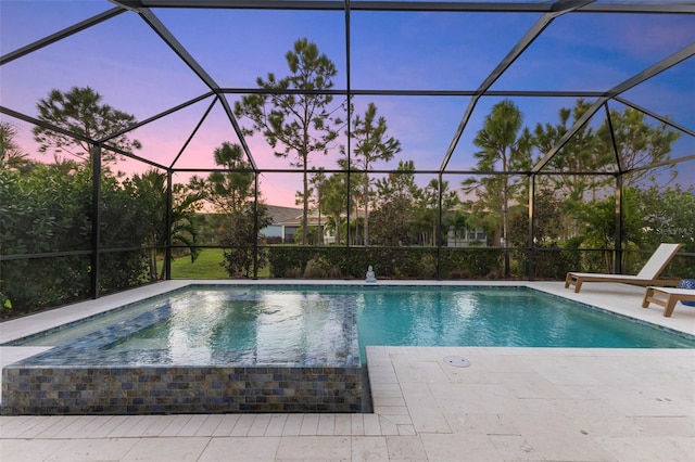 pool at dusk with glass enclosure and a patio area