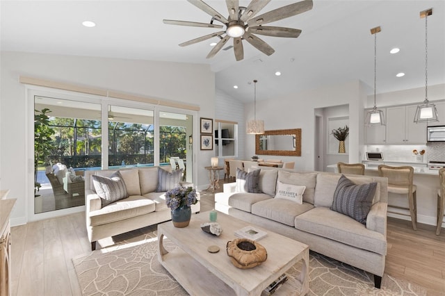 living room with ceiling fan, light hardwood / wood-style flooring, and vaulted ceiling