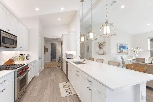 kitchen featuring appliances with stainless steel finishes, white cabinetry, hanging light fixtures, sink, and a breakfast bar