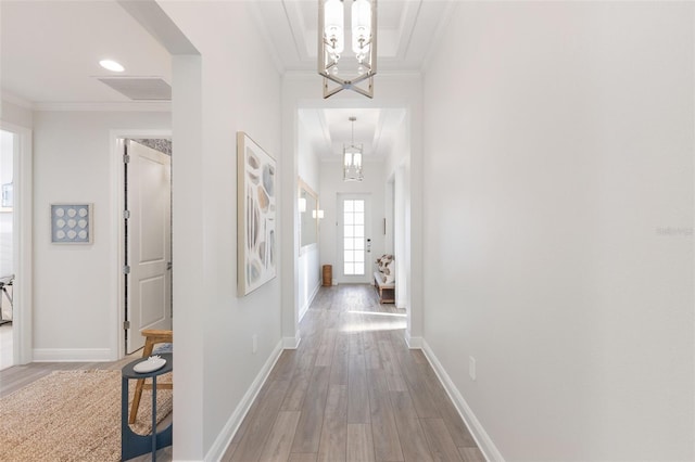 hallway with a notable chandelier, ornamental molding, and wood-type flooring