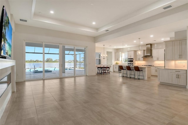 living room with a raised ceiling, an inviting chandelier, and light tile patterned flooring