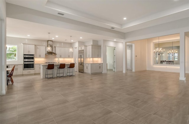 tiled living room featuring sink, a raised ceiling, and a chandelier