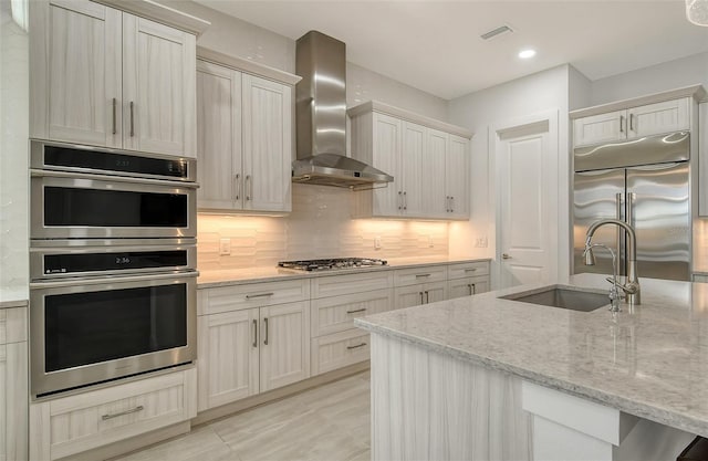 kitchen featuring wall chimney range hood, stainless steel appliances, sink, and light stone countertops