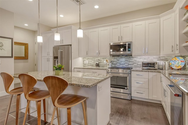 kitchen featuring tasteful backsplash, white cabinetry, a kitchen island, decorative light fixtures, and stainless steel appliances