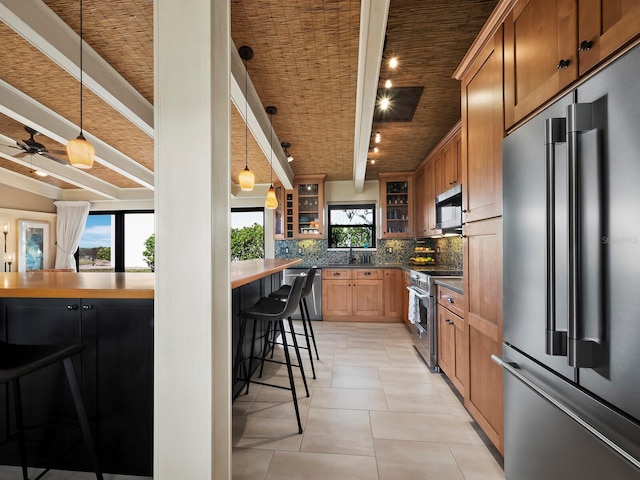 kitchen with a breakfast bar, a wealth of natural light, pendant lighting, beamed ceiling, and premium appliances