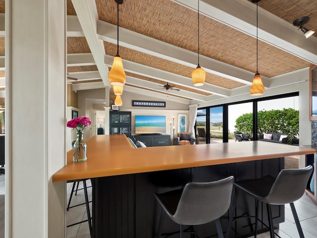 kitchen featuring light tile patterned flooring, ceiling fan, a kitchen bar, and lofted ceiling with beams