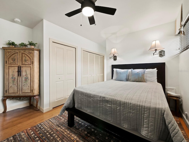 bedroom with hardwood / wood-style flooring, ceiling fan, and two closets