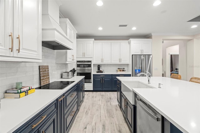 kitchen featuring premium range hood, white cabinets, blue cabinets, sink, and stainless steel appliances