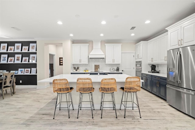 kitchen featuring custom exhaust hood, an island with sink, white cabinets, and appliances with stainless steel finishes