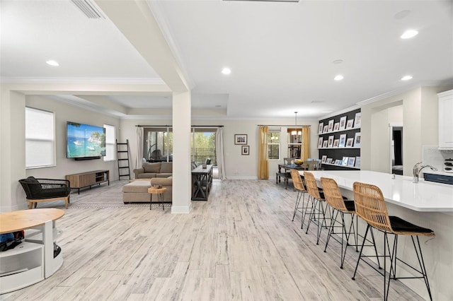 interior space featuring white cabinetry, light hardwood / wood-style floors, a breakfast bar, a tray ceiling, and crown molding