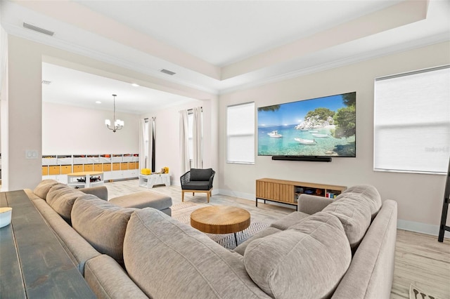 living room with ornamental molding, light hardwood / wood-style floors, a chandelier, and a raised ceiling