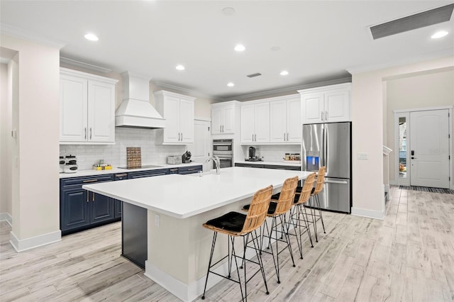 1012 Fernleaf Run, Bradenton, FL 34212 - kitchen with appliances with stainless steel finishes, premium range hood, blue cabinets, light wood-style flooring, and ornamental molding