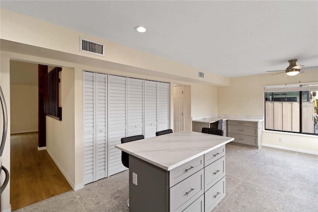 kitchen with gray cabinets, a kitchen island, light stone counters, and ceiling fan